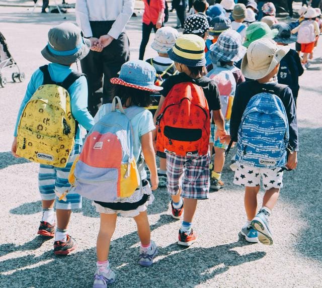 A group of young children wearing colorful backpacks and hats are walking together outdoors.