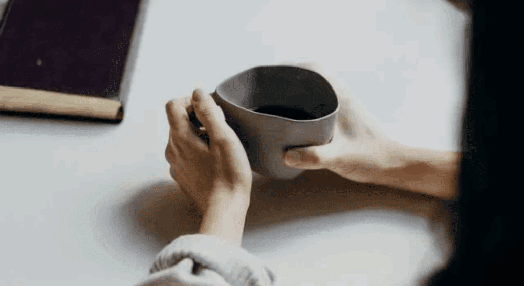 A person holding a mug of black coffee