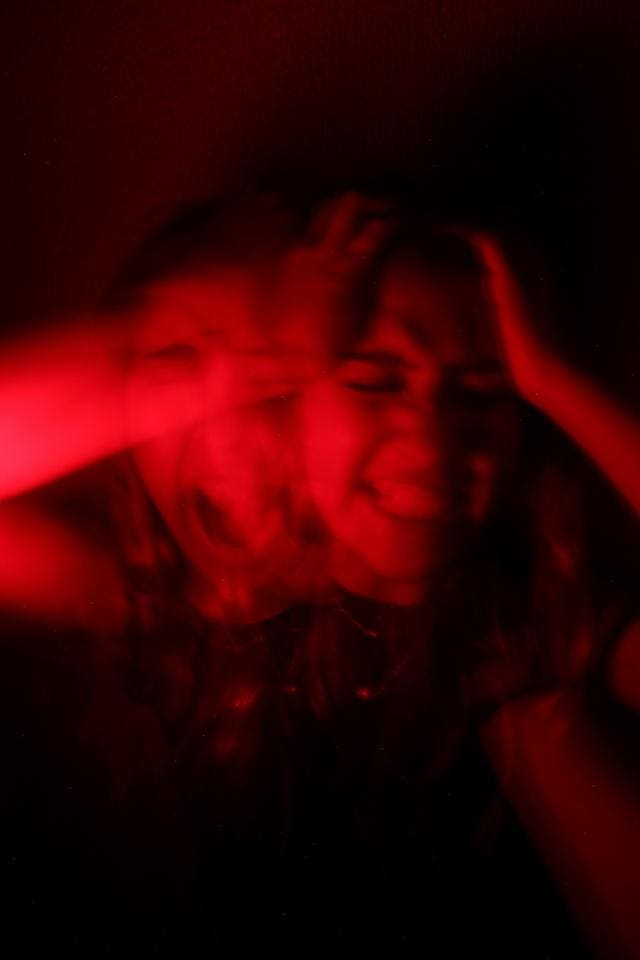 A person is holding their head with both hands, appearing stressed in a red-lit, blurred image.