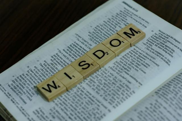 Scrabble tiles spelling "WISDOM" are placed on an open book.