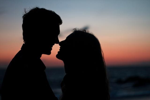 Silhouetted couple facing each other at a beach during sunset.