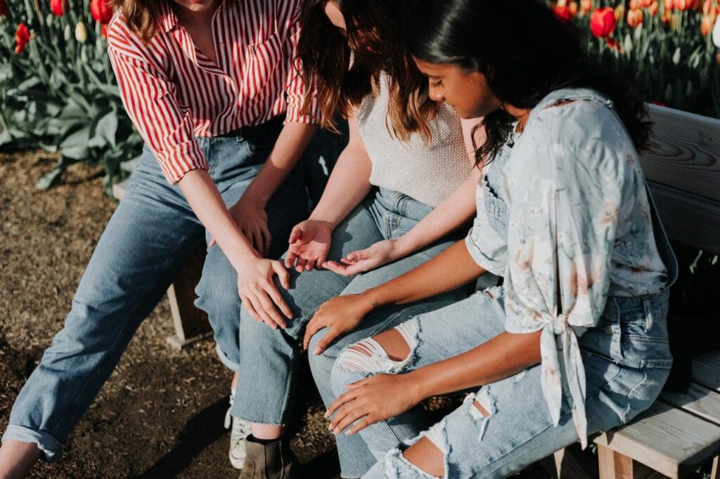 Three people sitting on a bench in a garden, examining something in one of their hands. They are surrounded by blooming tulips.