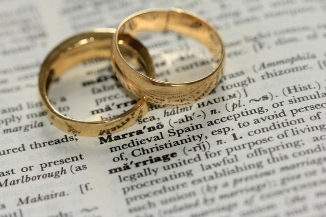 Two gold wedding rings resting on an open dictionary page showing the definition of "marriage.