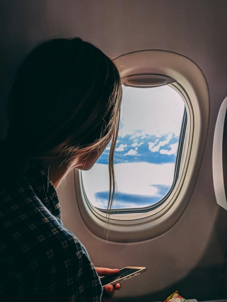 Person looking out an airplane window at clouds, holding a smartphone.