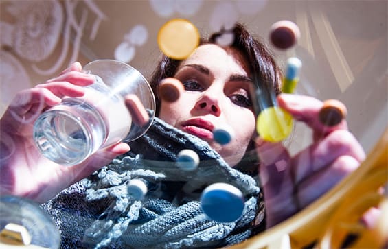 Woman looking at various pills floating in front of her while holding a glass of water.