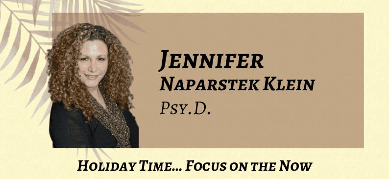A woman with curly hair and a black top appears next to text reading "Jennifer Naparstek Klein, Psy.D. Holiday Time... Focus on the Now" on a beige background with a leaf design.